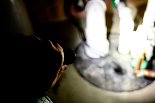 Plumber using flashlight to look inside sump pump.