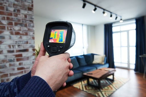 A man pointing a infrared camera at a wall in a home's living room.