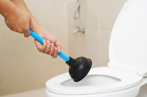 Homeowner using plunger to unclog toilet.